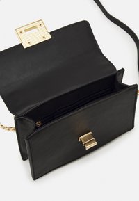 Černá kožená kabelka se zlatým kováním a zapínáním na klips. Uvnitř se nachází jedna kapsa na zip a několik přihrádek. Hladký povrch.