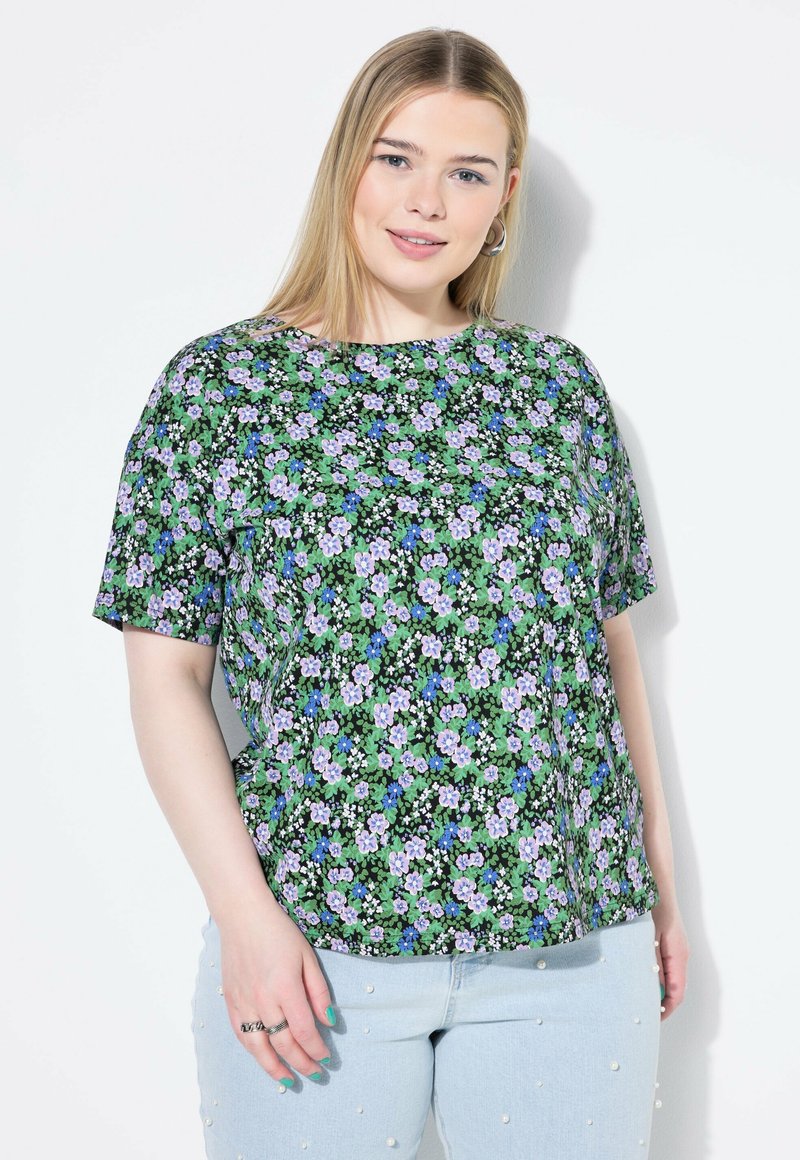Top de manga corta con un estampado floral que presenta flores moradas y azules sobre un fondo negro. El diseño tiene un escote redondo y un corte holgado.