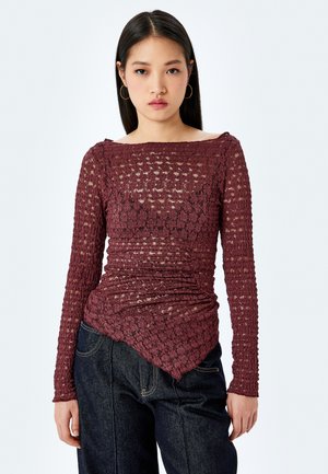 Bordeaux langærmet top lavet af tekstureret blonder, med bådudskæring, rynkede detaljer og en takkede kant, parret med mørke jeans.