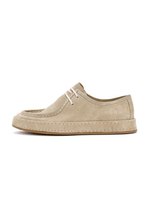 Chaussure en daim beige avec un bout rond, des coutures visibles et des lacets élastiques ; dotée d'une semelle en caoutchouc épaisse et texturée.