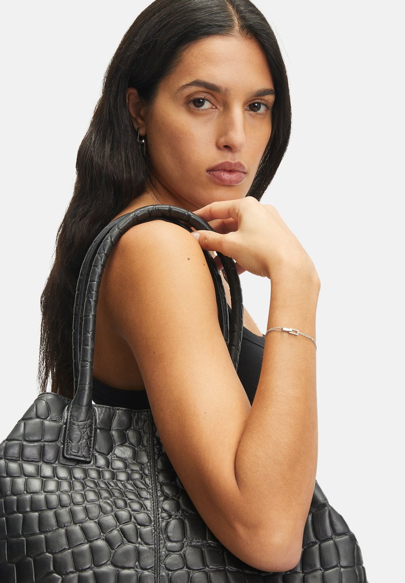Borsa a mano nera in pelle con una finitura testurizzata a effetto coccodrillo. Presenta manici allungati e un corpo spazioso. Sfondo bianco uniforme.