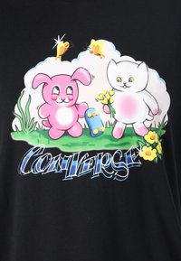 Schwarzer Stoff mit einem grafischen Motiv eines rosa Hasen und einer weißen Katze, umgeben von Blumen und Schmetterlingen, mit dem Text "CONVERSE" darunter in stilisierter Schrift.