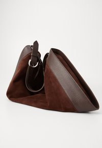 Sac à main en cuir suédé brun avec une sangle en cuir texturé et des accents. Le sac a un design décontracté, avec une large ouverture pour un accès facile.