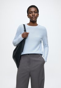 Hele sinine triibuline kampsun pikkade varrukatega, kombineeritud tumeda halli pükstega. Modell kannab musta nahast õlakotti.