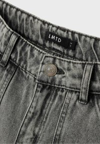 Jeans in denim grigio con una finitura texture, dotati di un bottone in metallo, passanti per cintura e un'etichetta con la dicitura "LMTD" contenente le informazioni sulla taglia.