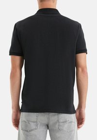 Zwarte polo met een klassieke kraag, korte mouwen en zijsplitten, gemaakt van zacht katoen. Grijze jeans zichtbaar bij de taille.