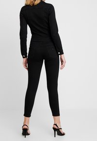 Black fitted jacket and skinny jeans, both made of denim. The jacket features a smooth texture and button details; the jeans have rear pockets.