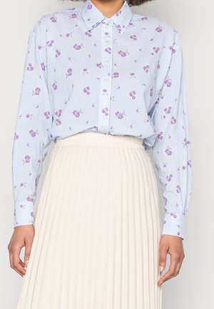 Camicia a righe blu chiaro con piccoli motivi floreali viola, colletto button-down e maniche lunghe, abbinata a una gonna plissettata color crema.