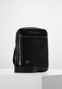 Borsa nera in pelle con una superficie liscia, dettagli blu, zipper anteriore, forma rettangolare e tracolla rimovibile.