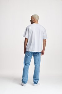 Witte katoenen t-shirt met korte mouwen, losse pasvorm, gecombineerd met lichtblauwe denim jeans. Sneakers zijn wit, met een gladde textuur en eenvoudig ontwerp.