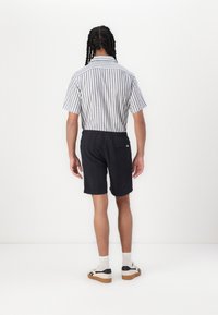 Korte mouwen gestreept shirt in blauw en wit, gecombineerd met donkere short. Bevat een elastische tailleband en een enkele achterzak. Casual schoeisel zichtbaar.