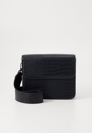 Mustatoon krokodilli tekstuuriga kotte, millel on ristkülikukujuline kuju, klapiga kaas ja eemaldatav rihm. Omab siledat pinda ja läikivat välimust.