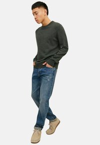 Dunkelgrüner Strickpullover mit Rundhalsausschnitt, kombiniert mit blauen Denim-Jeans und beigen Schuhen. Lockerer Schnitt mit gerippten Bündchen und Saum.