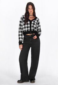 Cardigan a maglia a scacchi bianco e nero, design cropped con bottoni, abbinato a jeans neri a vita alta e stivali neri.