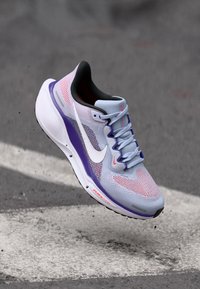 Chaussure de course légère avec un dessus en mesh bleu clair et violet, ornée d'un logo Swoosh blanc et d'une semelle rembourrée avec des accents multicolores.