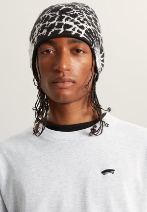 Bonnet en tricot avec un motif géométrique noir et blanc, associé à un sweat-shirt gris clair avec un petit logo de skateboard noir.