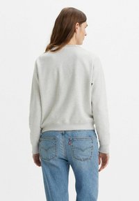 Lichtgrijze sweatshirt met een ribbelboord rond de hals, lange mouwen en een aansluitende zoom, gecombineerd met lichtblauwe spijkerbroek met achterzakken.