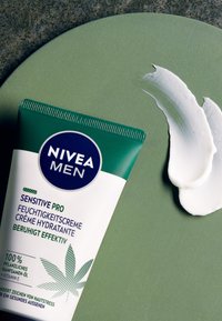 NIVEA Men Sensitive Pro moisturizing cream tube, green with white accents, placed on a green circular surface, with a white cream smear.
