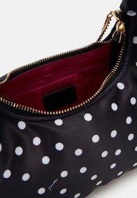 Czarna torebka w białe kropki, z złotym zamkiem błyskawicznym, czerwoną podszewką i małą kieszonką wewnętrzną. Gładki materiał, zaokrąglony kształt.