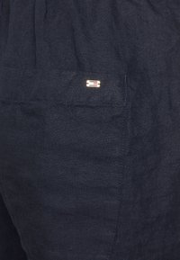 Navy blue linen shorts with a textured finish, featuring a small gold metal logo accent on the back pocket.