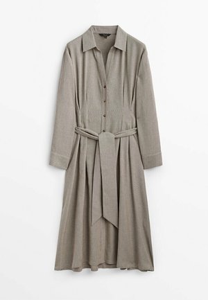 Robe chemise beige à manches longues avec col, boutons sur le devant, ceinture à nouer à la taille et jupe plissée suspendue sur fond blanc.