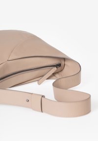 Beige Leder Crossbody-Tasche mit sichtbarem schwarzen Reißverschluss und passendem Leder-Reißverschlussanhänger, ausgestattet mit einem breiten verstellbaren Tragegurt.