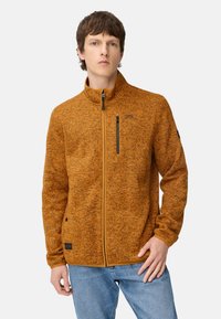 Pomarańczowa kurtka polarowa z wysokim kołnierzem, zamkiem błyskawicznym z przodu i czarną kieszenią na zamek. Charakteryzuje się fakturowaną tkaniną i kontrastującymi akcentami zamków.
