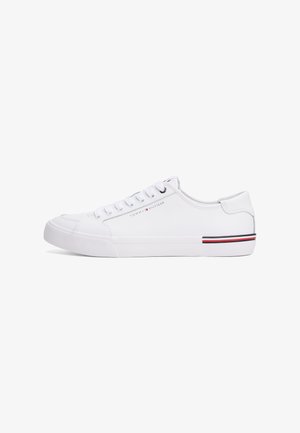 Zapatilla blanca de corte bajo con cordones blancos, logo sutil de Tommy Hilfiger en el lateral y detalle de franjas roja, blanca y negra en el tacón de la suela.