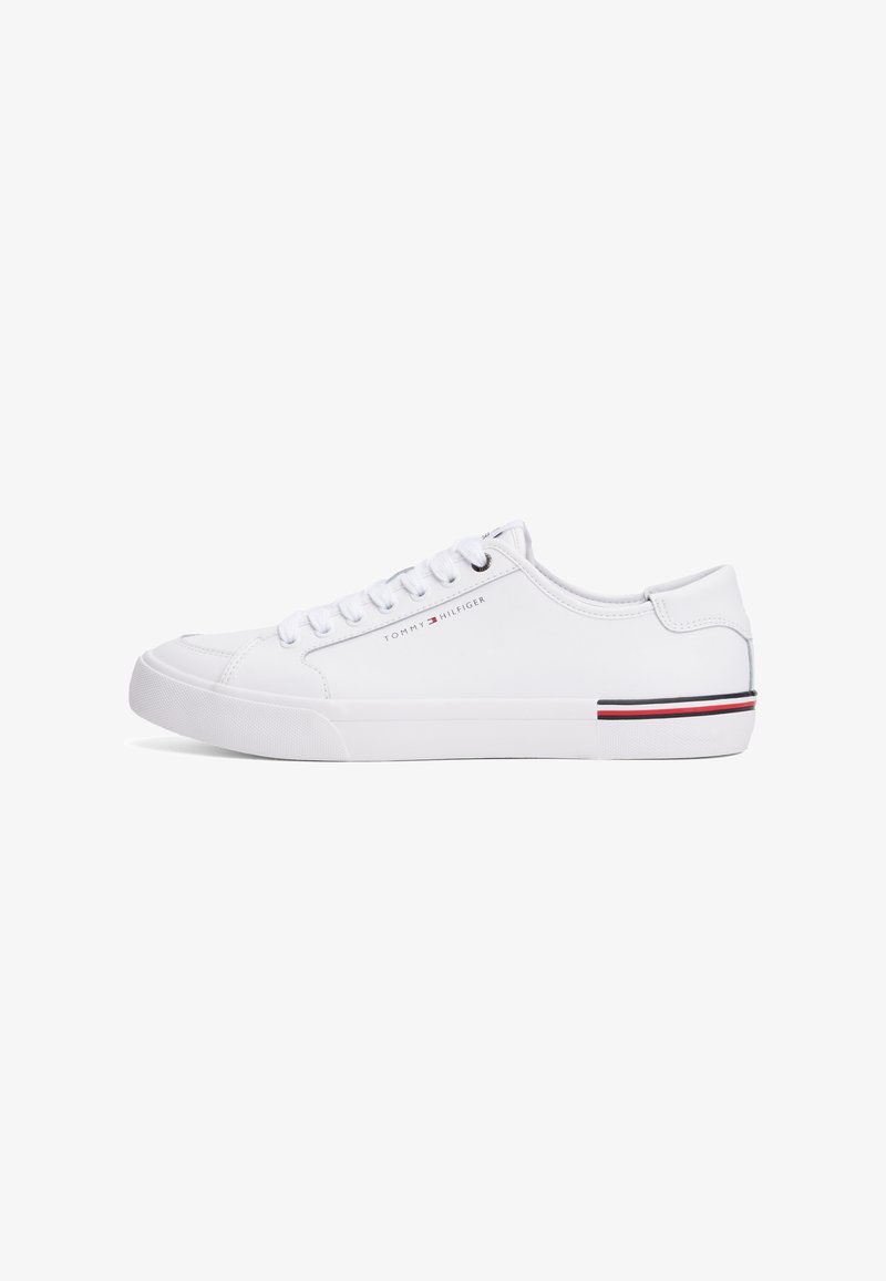 Baskets basses blanches avec lacets blancs, logo subtil Tommy Hilfiger sur le côté, et détail de rayures rouge, blanc et noir à l'arrière de la semelle.