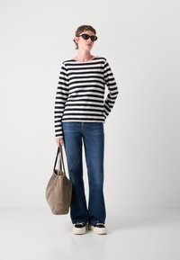 Stripet langermet topp i svart og hvitt, blå jeans og en beige semsket skinn veske. Modellen har på seg svarte solbriller og plattform sneakers.