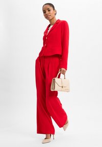 Rote maßgeschneiderte Blazerjacke mit passender weiter Hose, ergänzt durch eine beige Handtasche und nude-farbenen High Heels. Glattes Material mit strukturierter Gestaltung.