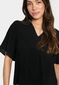 Blusa nera, con texture, dal collo a V, maniche a farfalla corte e una vestibilità ampia, con dettagli arricciati sotto il petto.
