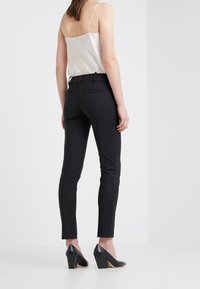 Černé elegantní kalhoty se slim fit, s hladkým povrchem, zadními kapsami a zkrácenou délkou. Doplněné černými vysokými podpatky.