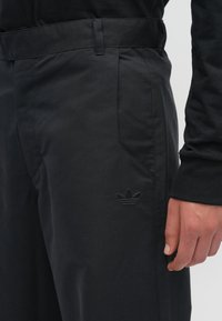 Pantaloni neri realizzati in tessuto morbido con vita aderente, dotati di tasche laterali e logo ricamato sulla coscia sinistra.