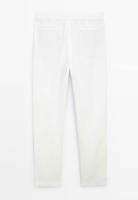 Pantalon blanc sur mesure avec une ceinture élastique et deux poches passepoilées à l'arrière, vu de dos sur un fond uni.