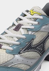 Λευκό και μπλε αθλητικό παπούτσι από δίχτυ με λευκά κορδόνια, μαύρο και κίτρινο λογότυπο στη γλώσσα και μαύρο στυλιζαρισμένο σχέδιο στο πλάι.