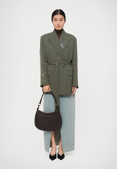 Blazer over taglia verde oliva con cintura, ricamo blu, abbinato a pantaloni beige a gamba larga in denim chiaro, borsa nera intrecciata e scarpe con punta.