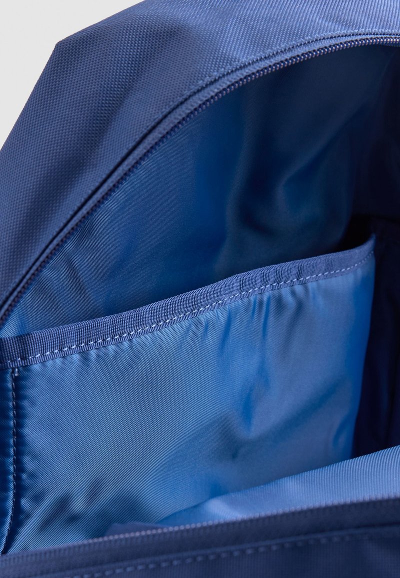 Interior de mochila de tela azul con bolsillo interno cosido y abertura de cremallera visible.