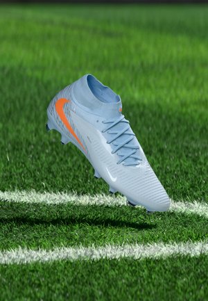 Crampon de football bleu clair avec un swoosh Nike orange flottant au-dessus d'un terrain en herbe verte avec des lignes blanches.