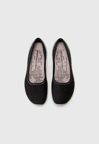Scarpe nere slip-on con tomaia in tessuto liscio, suola grigia e soletta rosa con motivi di ventilazione a pois. Design a punta arrotondata.