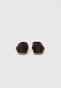 Καφέ σουέντ παπούτσια με στρογγυλεμένο σχήμα, φτιαγμένα με επίπεδη σόλα και μικρή λεπτομέρεια φιόγκου στην επάνω πλευρά. Λείο υλικό με ελάχιστες διακοσμήσεις.