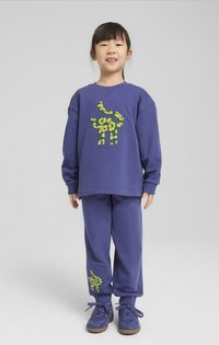 Conjunto de sudadera y pantalones morados con detalles de estampado de animales en amarillo y verde. La tela parece suave; el diseño es informal con puños acanalados.