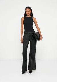 Canotta nera a coste abbinata a pantaloni neri a vita alta con gamba larga. Tiene una pochette nera. Tessuto liscio e design sartoriale.