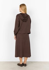 Brauner Kapuzenpullover mit Kapuze und weiten Ärmeln, kombiniert mit einem passenden Rock mit glatter Textur, von hinten gesehen.