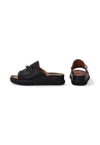 Zwarte leren slidesandalen met een knoopdetail op de bovenkant, voorzien van een gestructureerde zwarte zool en een lichtbruine voetbed.