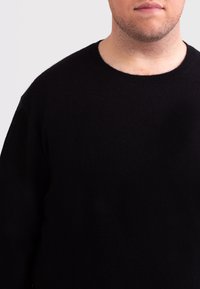 Maglione nero a maglia con colletto rotondo, caratterizzato da una texture morbida e maniche lunghe, che mostra un design semplice e senza cuciture.