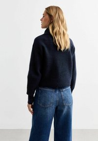 Marinblått ylletröja med hög krage och avslappnad passform. I kombination med medelhöga blå denimjeans. Mjuk textur och boxig form.