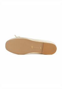 Chaussure plate beige avec une texture lisse, un bout rond et un détail en ruban fin sur le talon. Semelle en caoutchouc avec des stries horizontales et une étiquette de taille en relief.