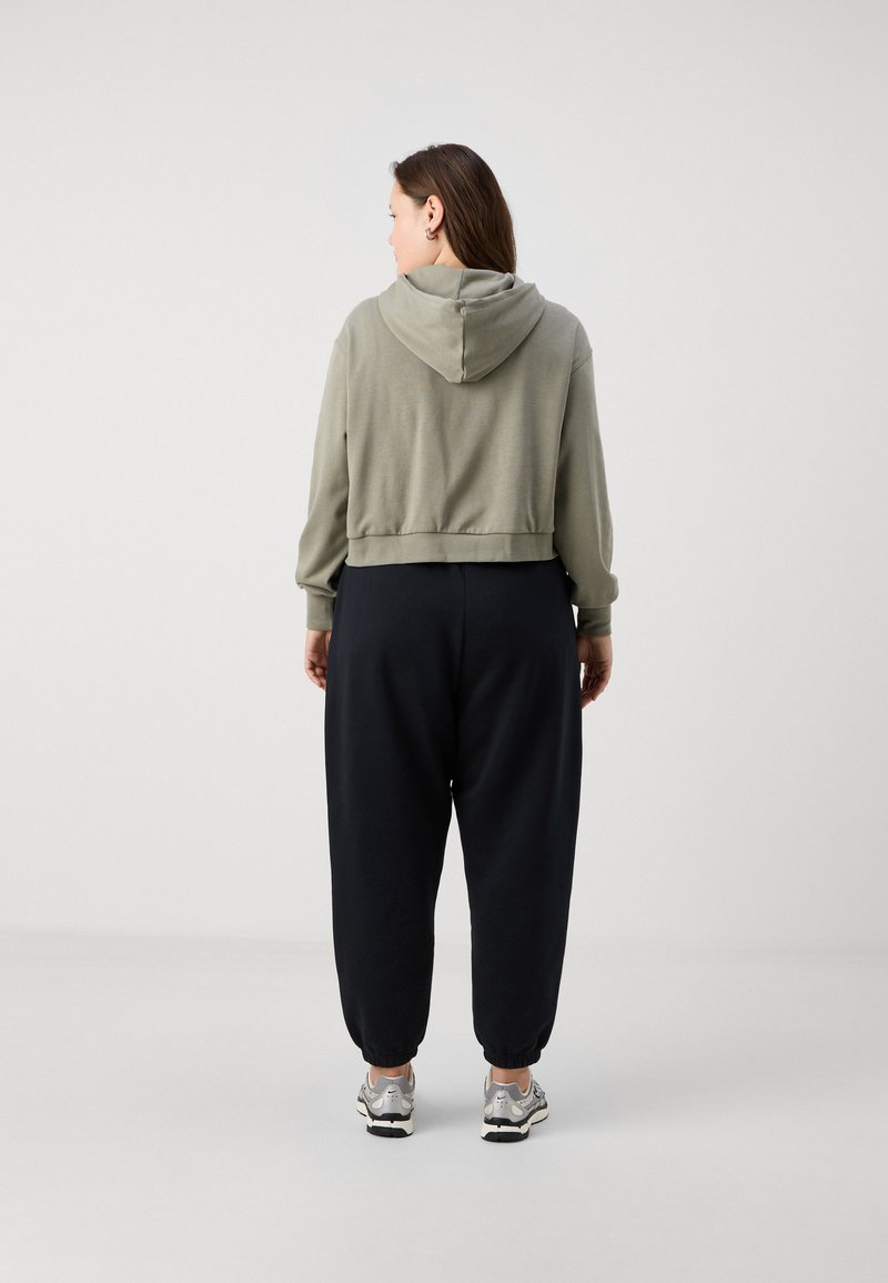 Sudadera verde oliva clara recortada con detalle en la costura trasera, combinada con pantalones negros holgados y cónicos. El material parece suave y casual, adecuado para el ocio.