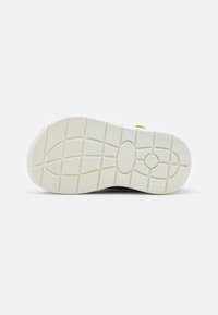 Shoe sole with textured white rubber, featuring a flexible design and a central logo. Smooth edges and deep grooves for traction.